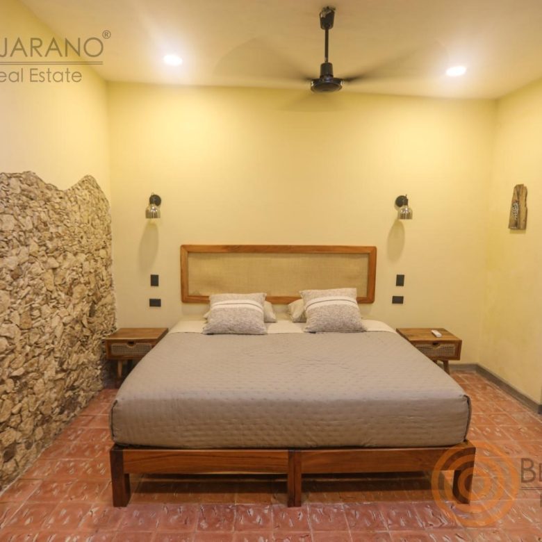 Recámara con muro de piedra, cama y ventilador de techo