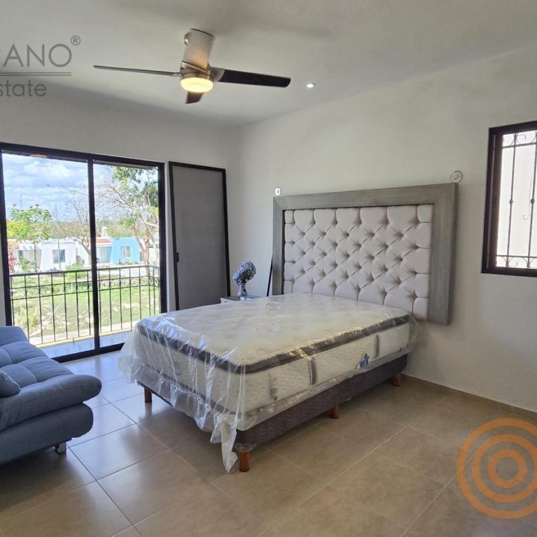 Recámara con cama, sillón azul y ventana al balcón