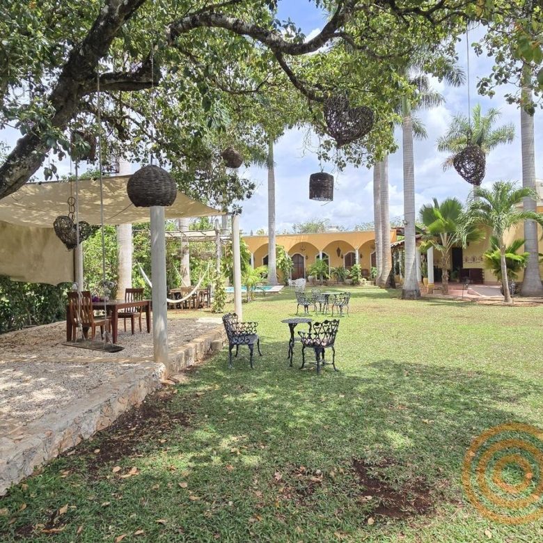 Jardín con mesas y árboles frente a los edificios del hotel