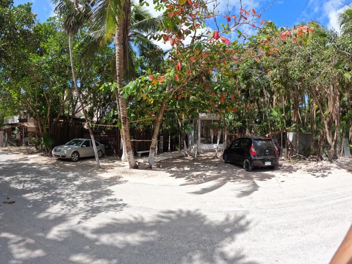 bre-pila-tul23-03 Calle de acceso al terreno en Tulum con vegetación y autos estacionados