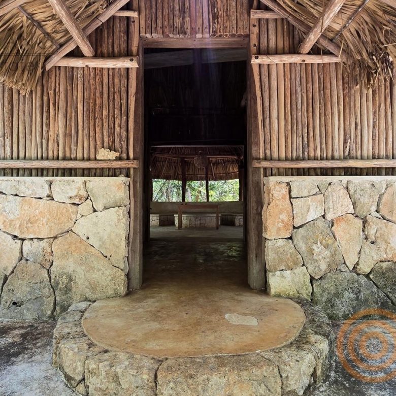 Entrada de la palapa con muros de piedra y madera