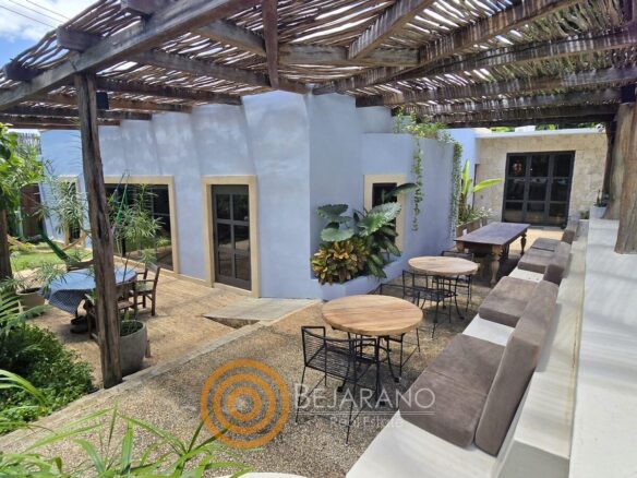 Terraza techada con pérgola de carrizo y mesas junto a la casa