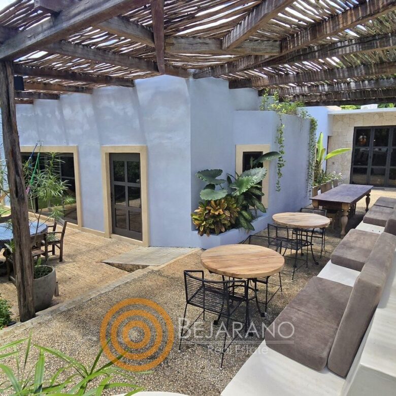 Terraza techada con pérgola de carrizo y mesas junto a la casa