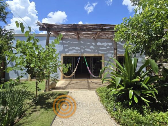 Andador entre jardín tropical hacia el porche con hamacas