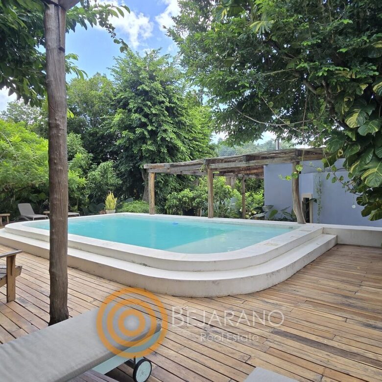 Alberca rodeada de árboles con camastros sobre deck de madera
