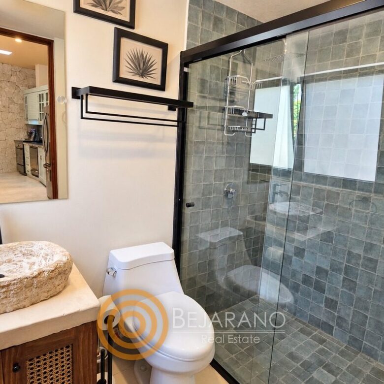 Baño con regadera de azulejo gris, lavabo de piedra y cuadros de agave
